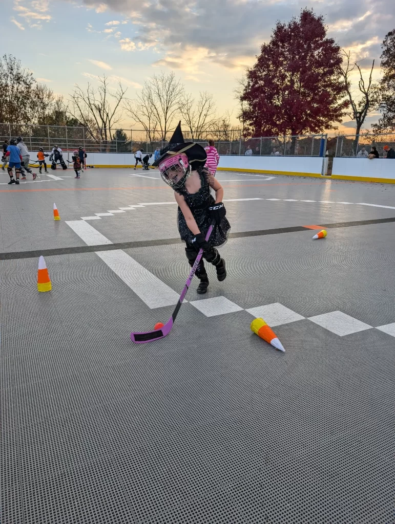 Hockey Halloween event with little girl dressed as a witch doing a stickhandling drill